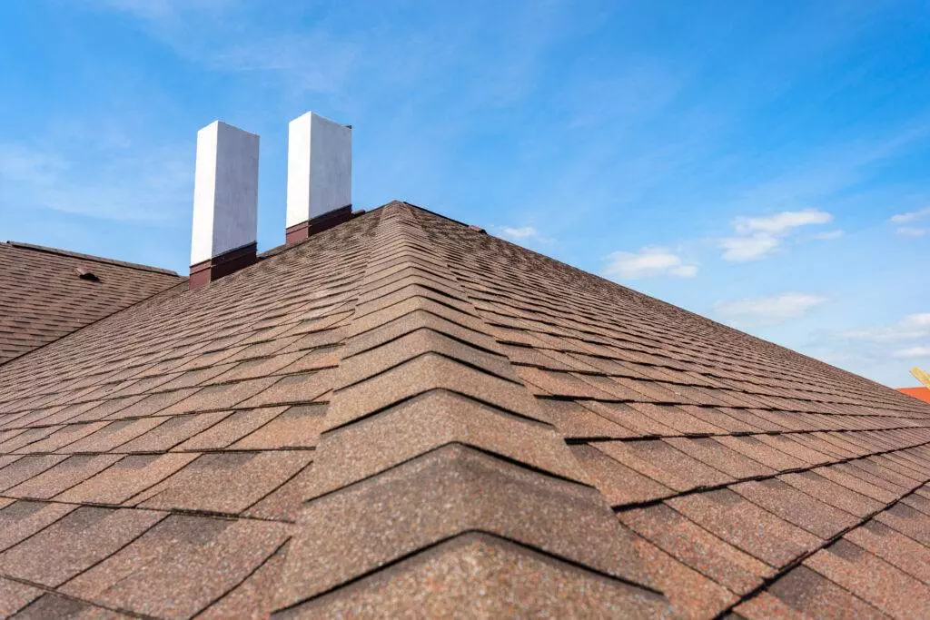 new roof with asphalt tile and two white chimney on new home under construction, against blue sky